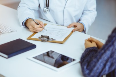 Arzt und Patient besprechen am Tisch sitzend ein Dokument