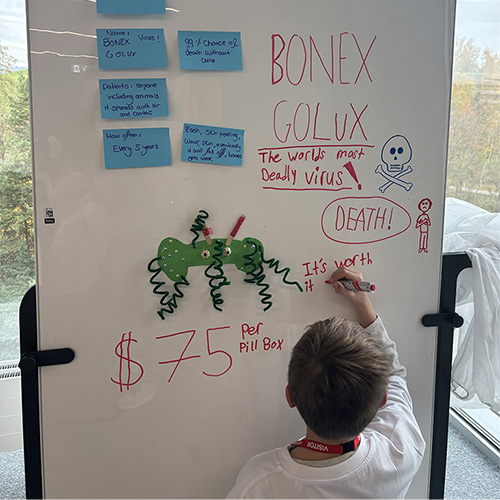 Photo: Kind schreibt auf ein Whiteboard voller Notizen und Zeichnungen über ein erfundenes Virus.